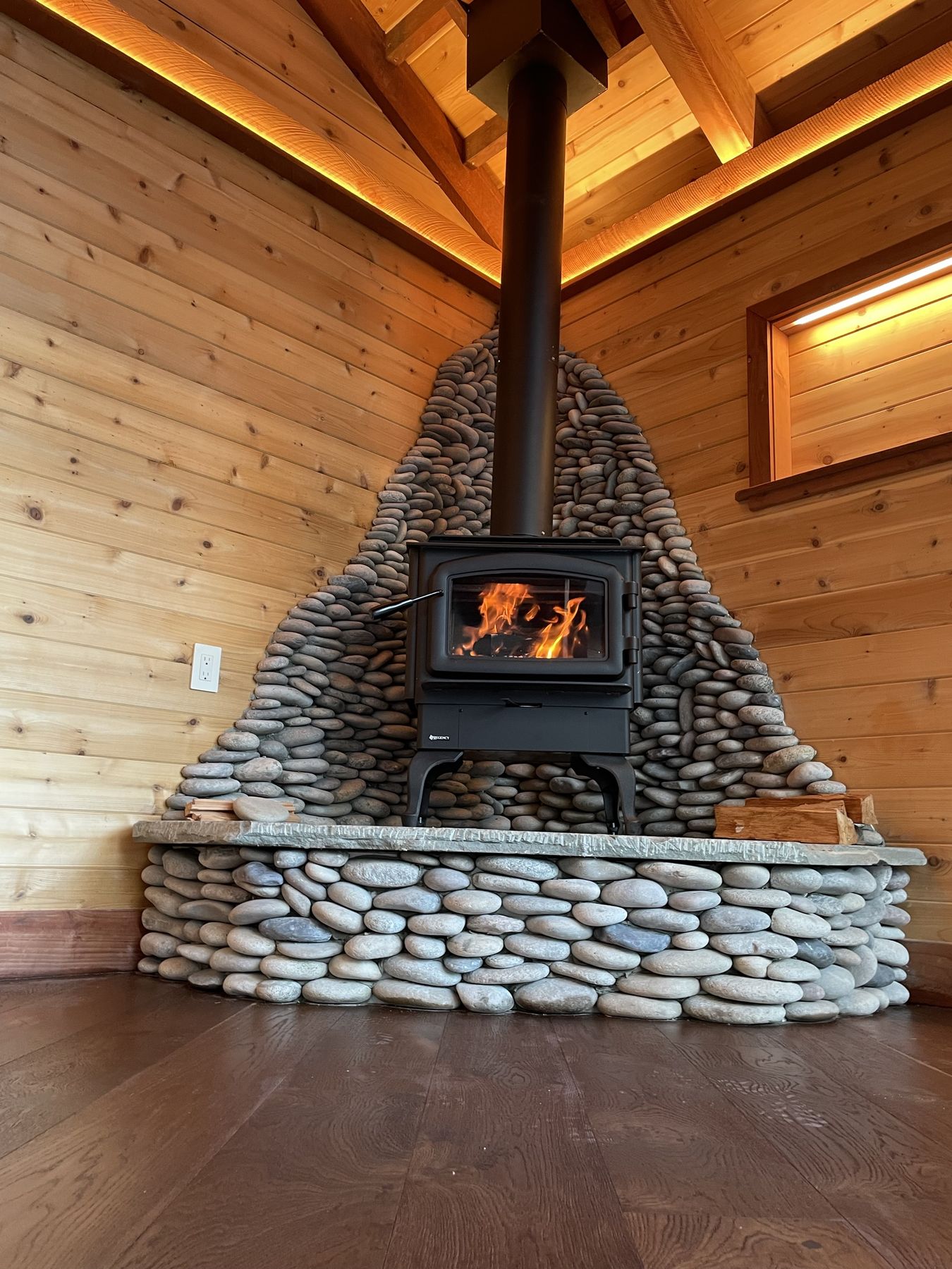 River-rock wood stove hearth inside a custom cedar studio built by EMC